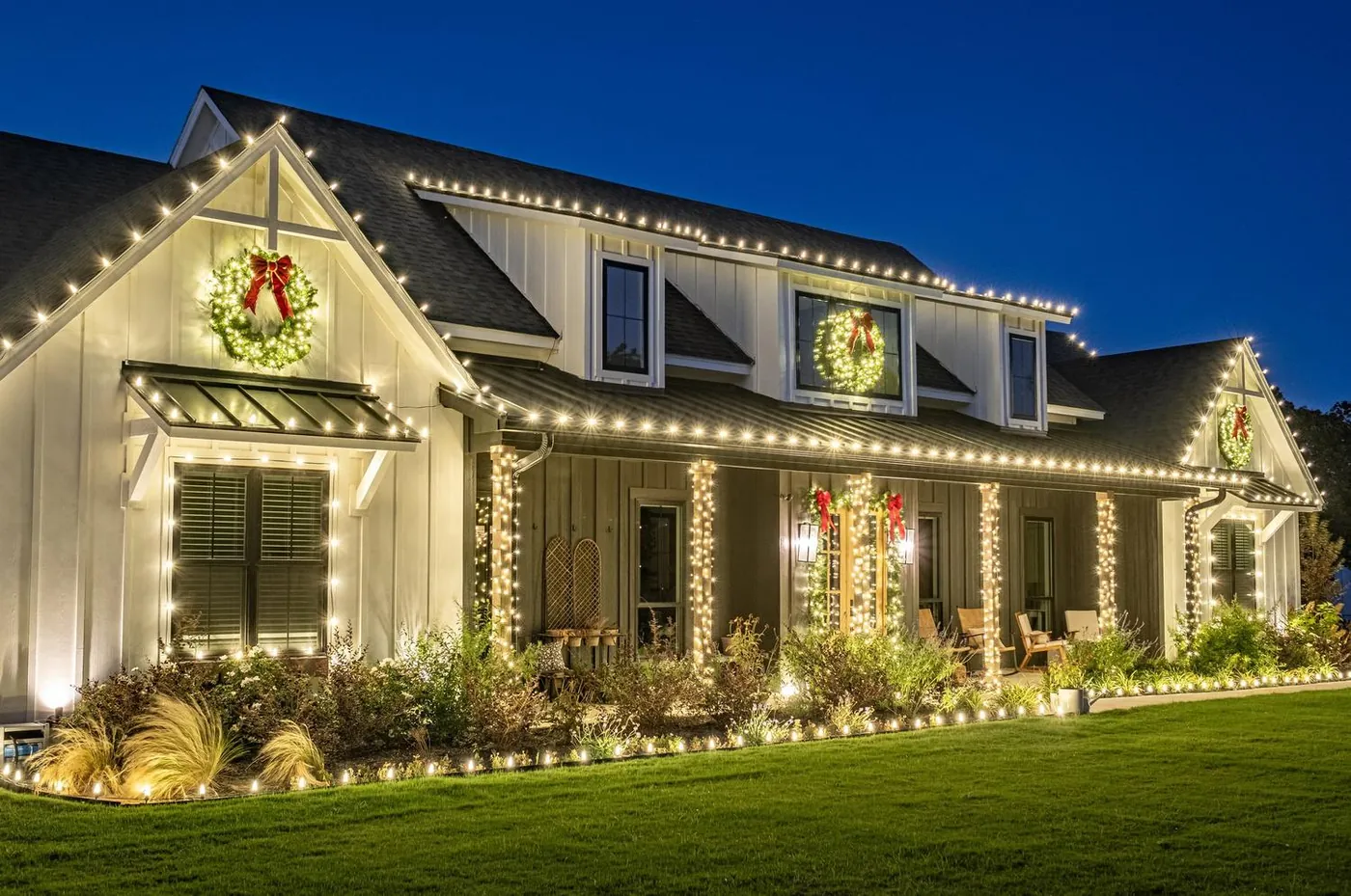 Modern farmhouse with Christmas lights along the roofline and wreaths at night